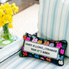 Needlepoint pillow by Furbish brand with bright colors and phrase 'what a long strange trip its been' on a blue and white striped chair