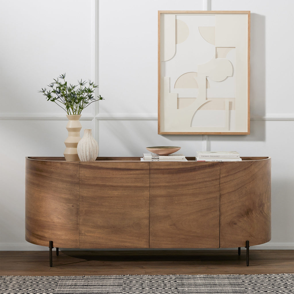 Curved wood 'Lunas' sideboard with small steel feet  by four hands furniture in a white walled room with modern art above and decorative items