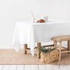 White linen table cloth on a wood table in room with white walls and seagrass rug