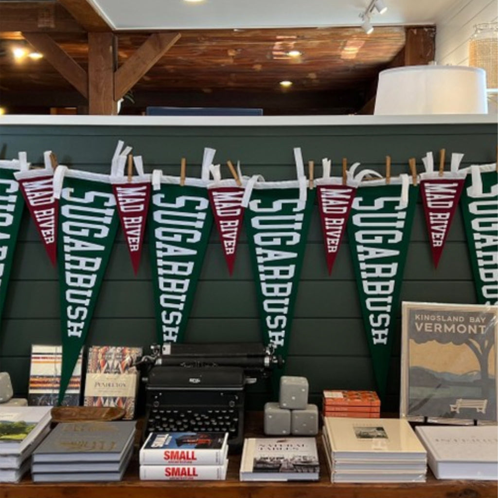 Mad River and Sugarbush pennants hanging on a green wall with books on a shelf below