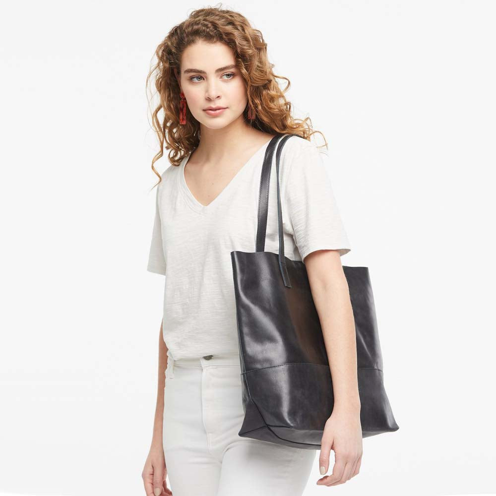 Model wearing Able brand Mamuye tote in black leather on a white background
