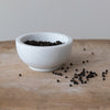 White marble bowl with peppercorns on a wood surface