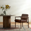 Brown leather 'Markia' arm dining chair with wood frame by four hands furniture on a patterned rug next to a round dining table