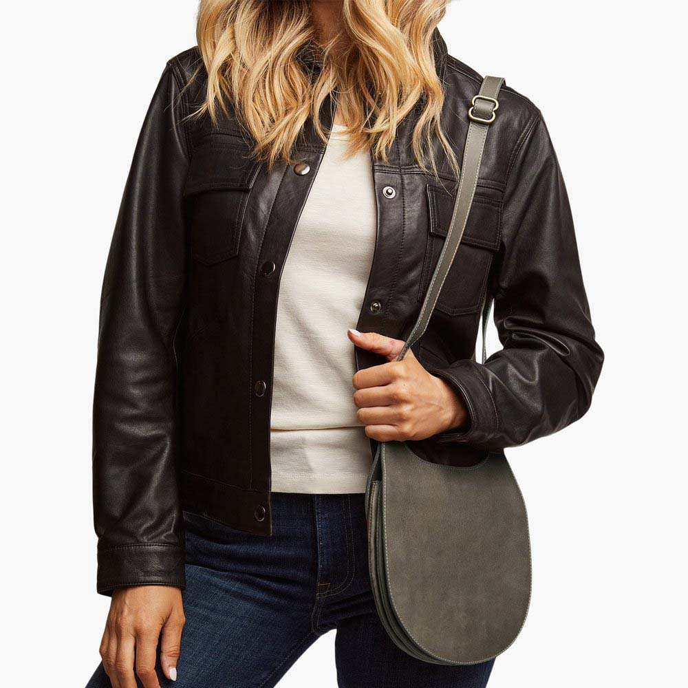 Model wearing Able brand Martha saddle bag in slate color with adjustable shoulder strap on a white background