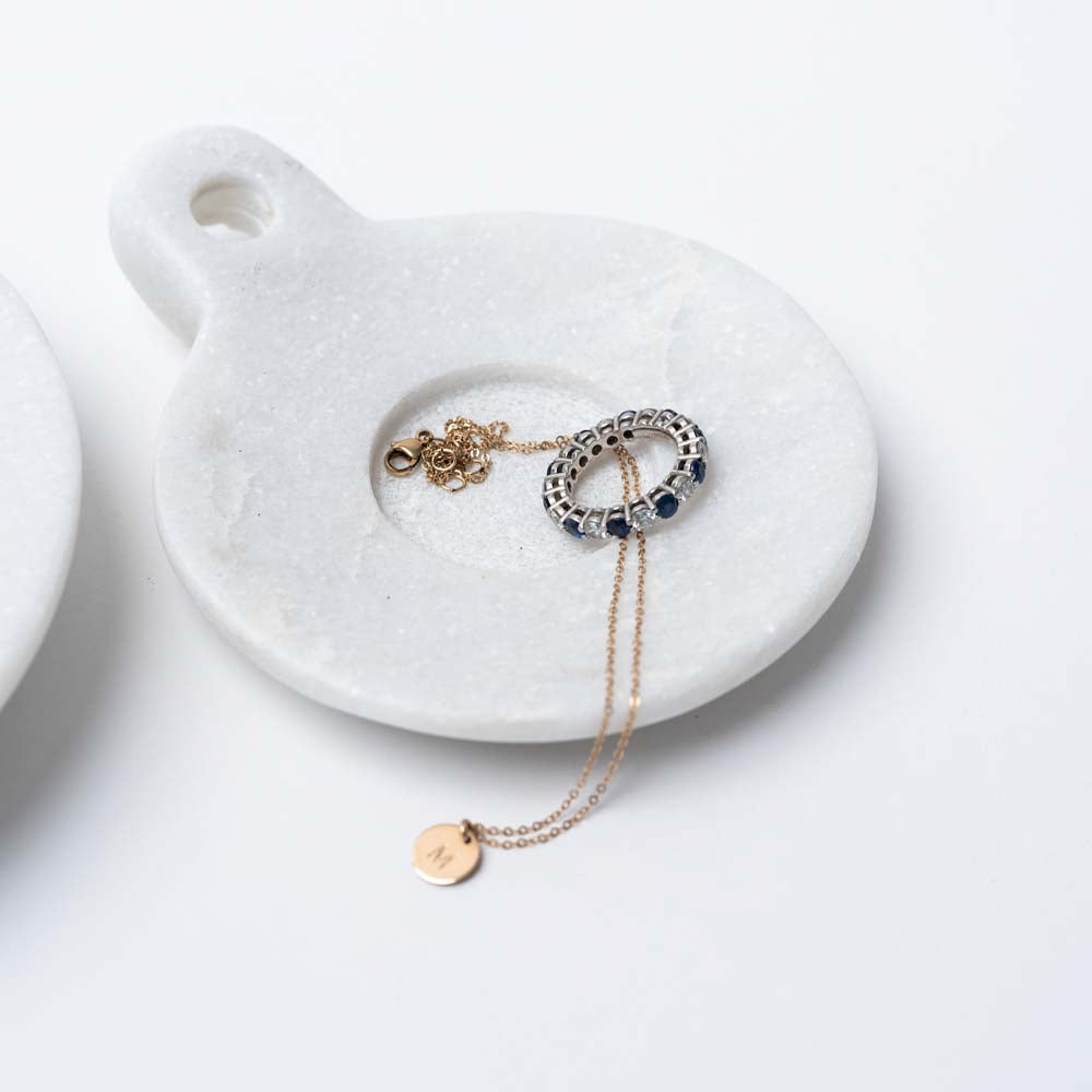 White marble dish with handle and jewelry inside on a white background