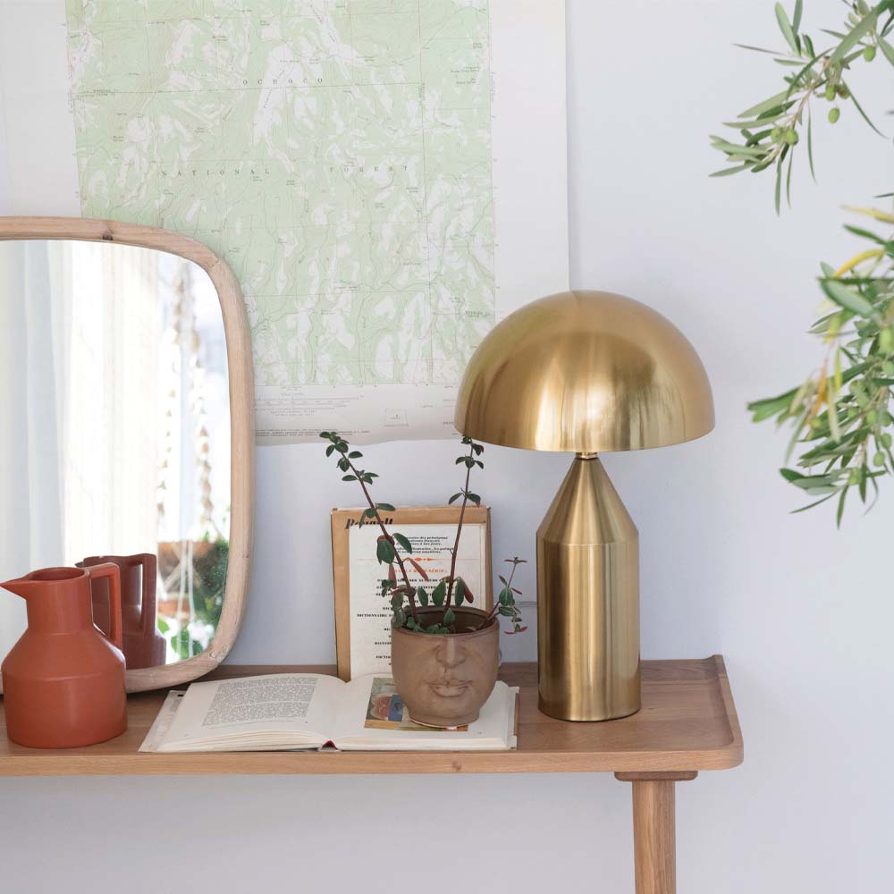 Brass finish table lamp with metal mushroom shade on a wood table with plants and books