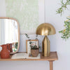 Brass finish table lamp with metal mushroom shade on a wood table with plants and books