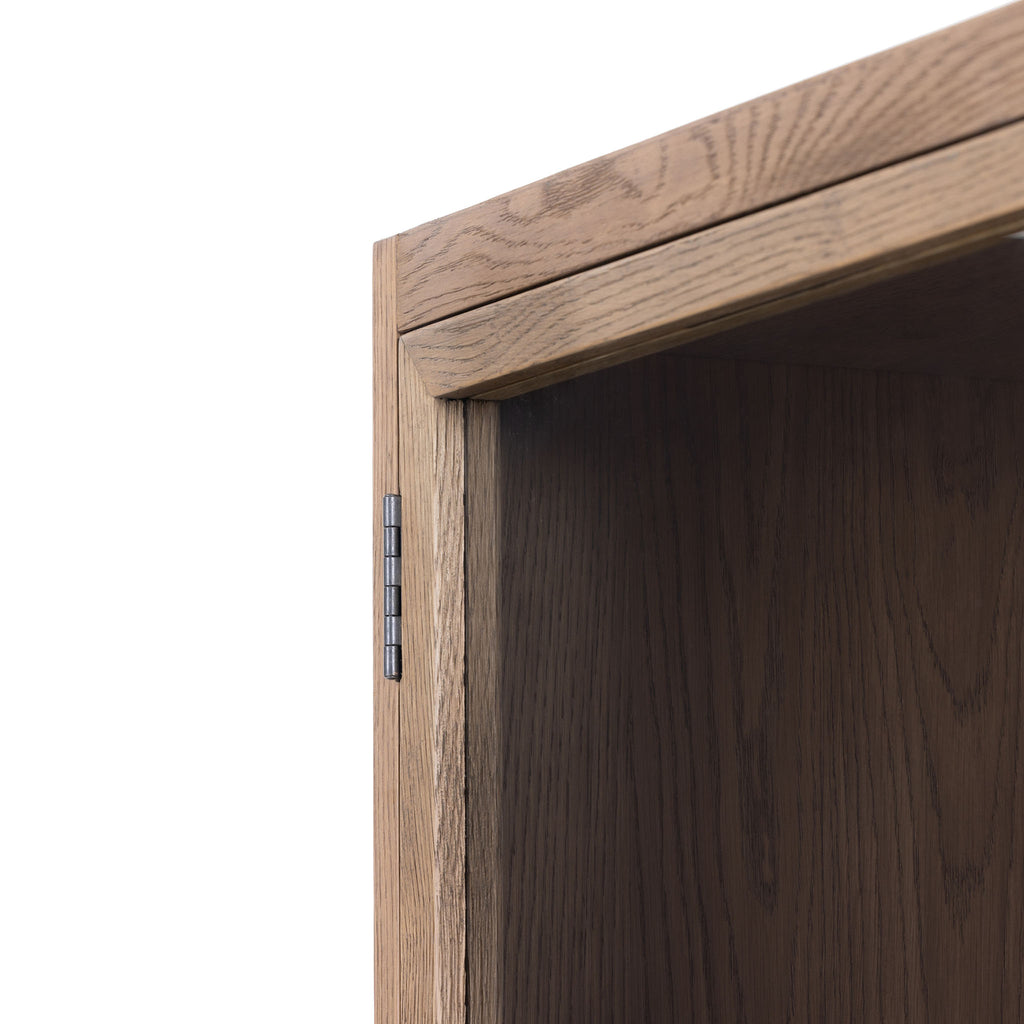 Close up of wood corner on Four hands furniture brand Millie oak cabinet with glass door against a white background