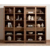 Two decorated Four hands furniture brand Millie oak cabinet with glass doors and four shelves side by side on a wood floor against a white wall