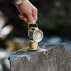 Hand holding barebones brand brass miner's lantern on a log 