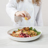 Female chef in white jacket squeezing lemon over chicken salad in Classic White Serve Bowl by fortessa on a white background