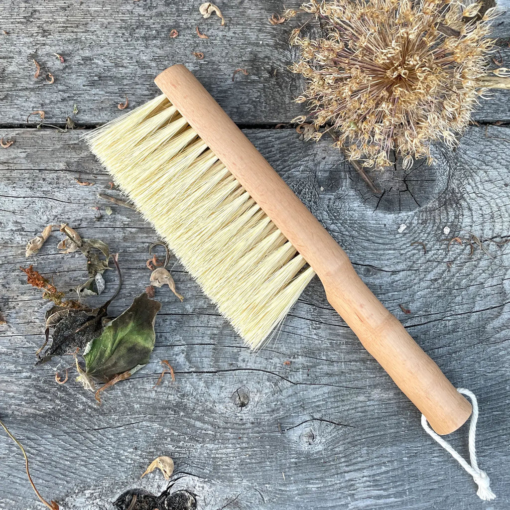 Gardening brush on a wood surface next to dried flowers and leaves