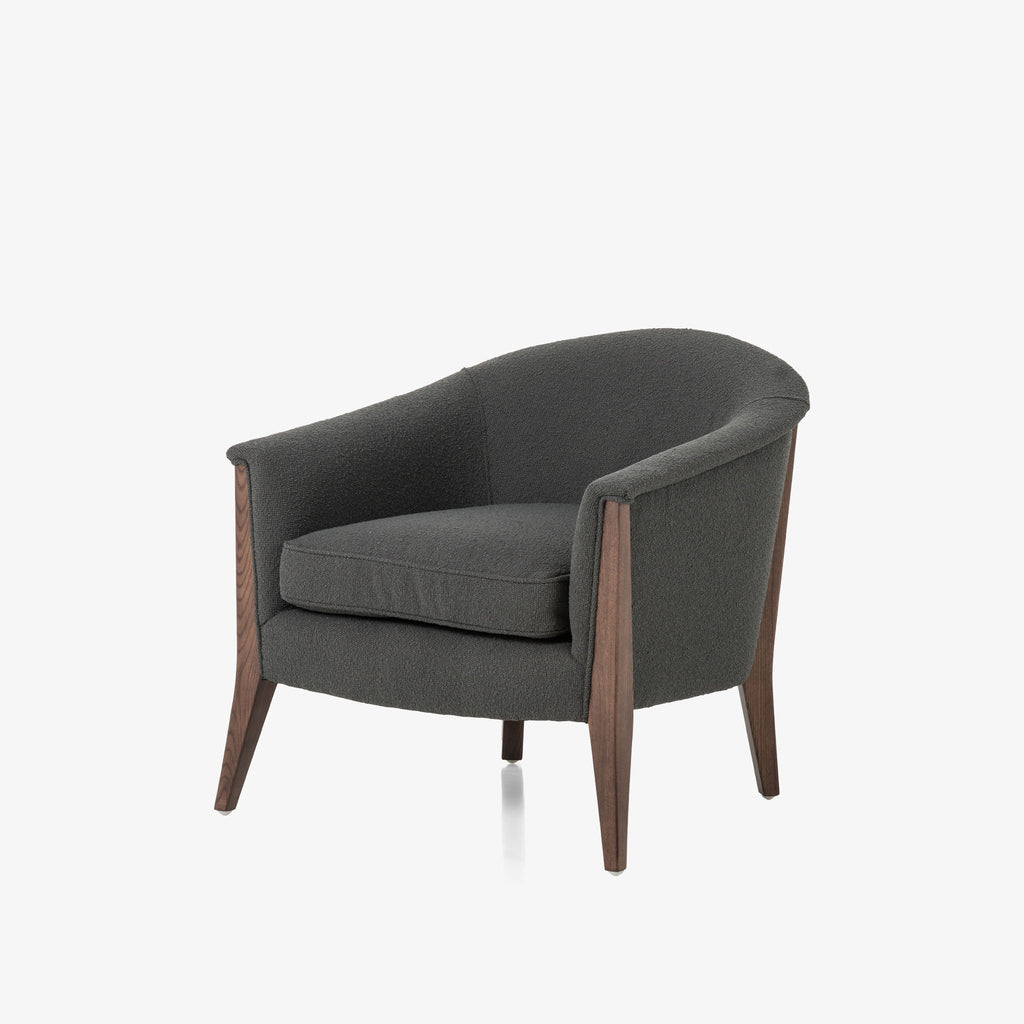 Grey upholstered 'nomad' arm chair by Four Hands Furniture with dark wood frame and rounded back on a white background