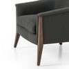 Grey upholstered 'nomad' arm chair by Four Hands Furniture with dark wood frame and rounded back on a white background