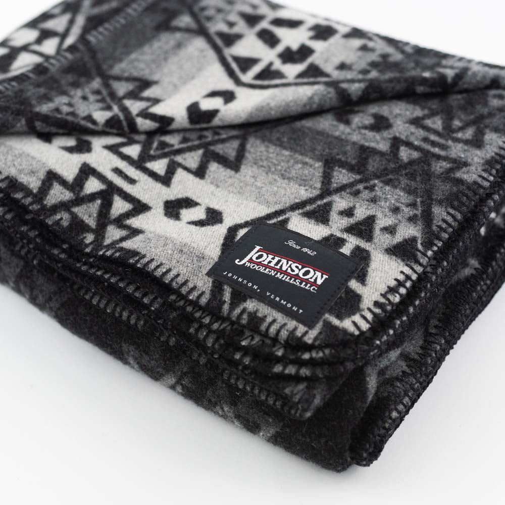 Close up of Johnson Woolen Mills wool blanket in charcoal grey aztec print on a white background  
