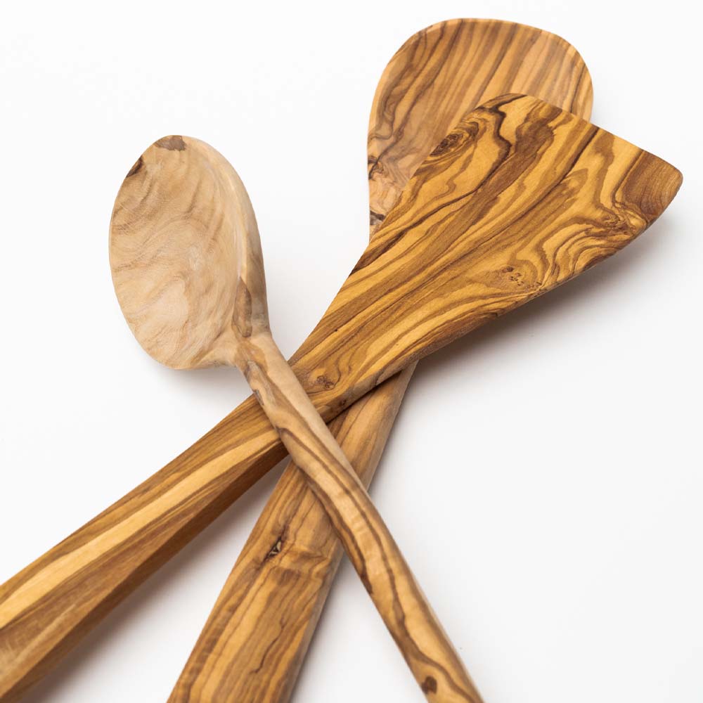 Three olive wood utensils stacked on a white background including spatula, large spoon and spoon with round head