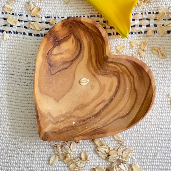 Olive Wood Heart Dish on a fabric surface with oatmeal and a flower scattered about