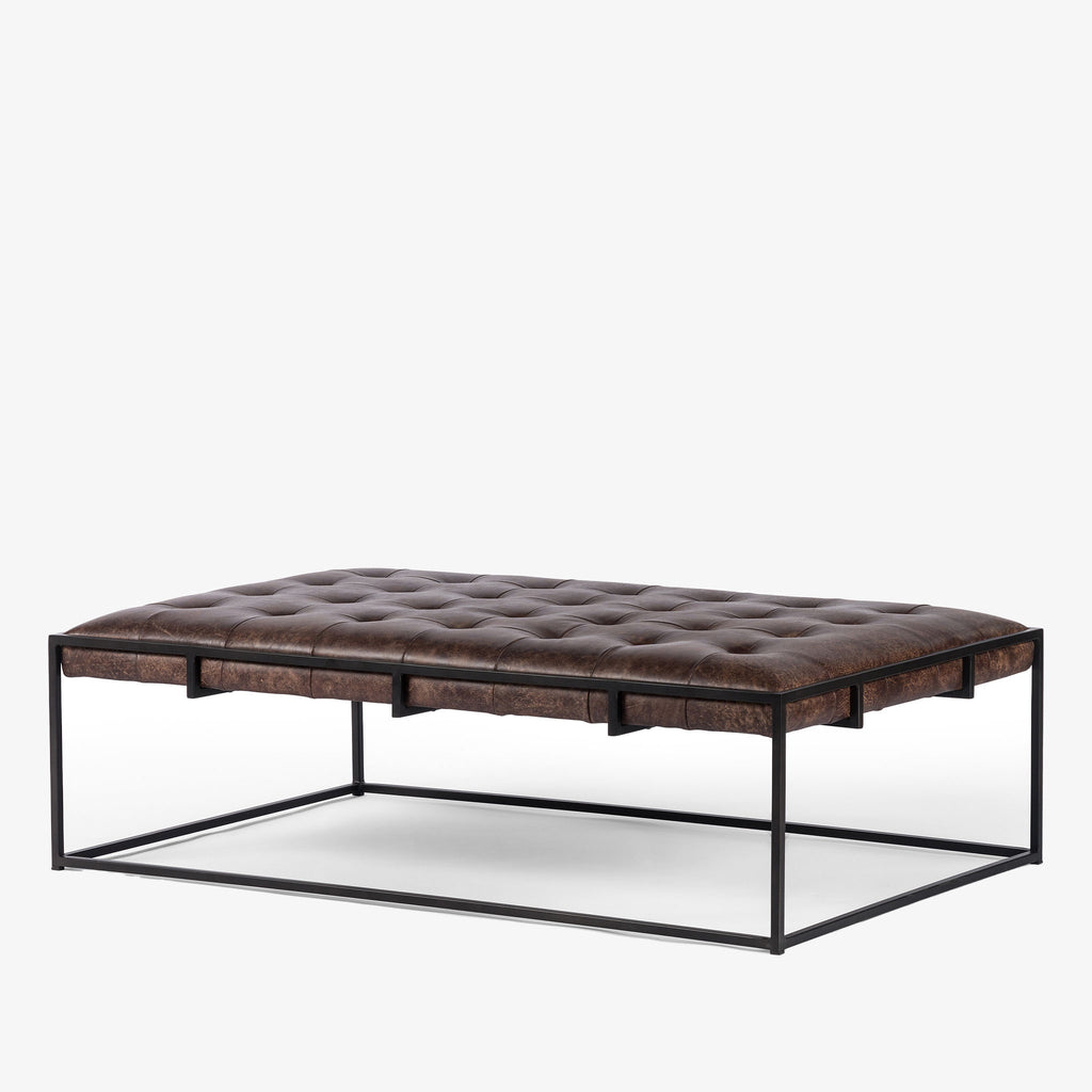 Four hands brand Oxford rectangular coffee table with black iron frame frame and distressed brown leather top on a white background
