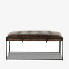 Four hands brand Oxford square coffee table with black iron frame frame and distressed brown leather top on a white background