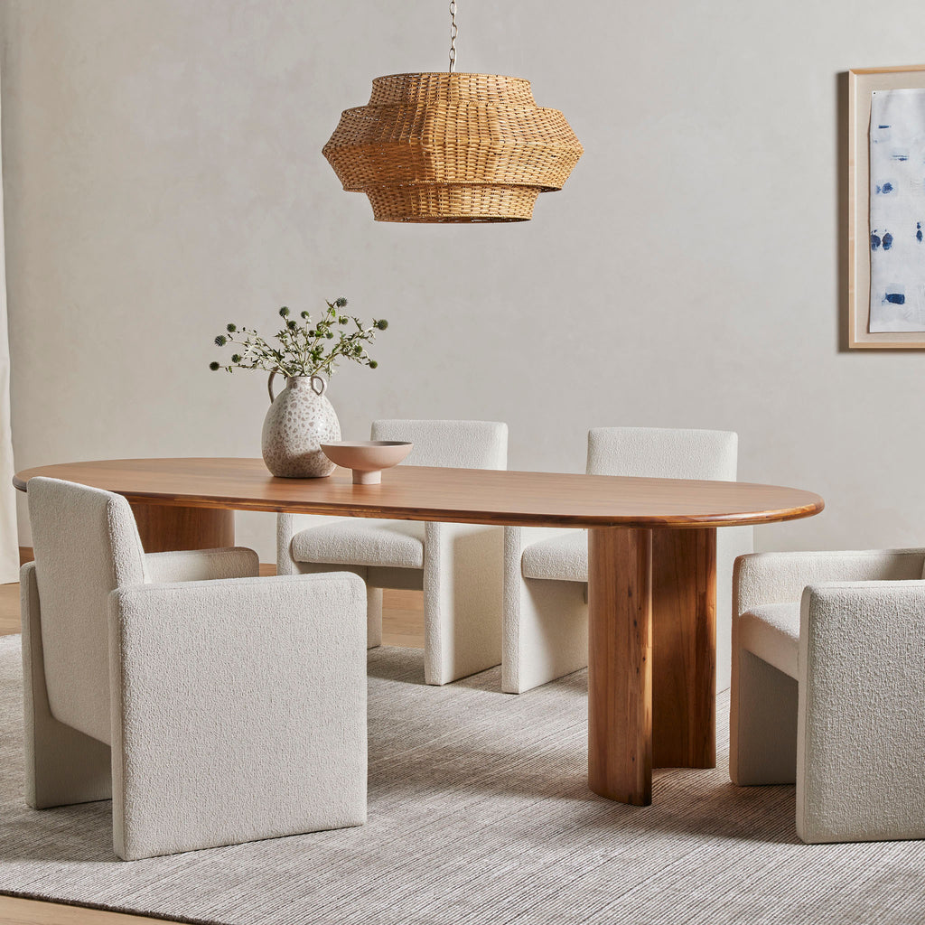 Dining room with grey rug and walls and rattan lamp with Light wood 'Paden' oval dining table by Four Hands Furniture with two legs 