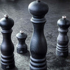 Various sizes of Peugeot Brand graphite pepper mills on black surface