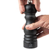 Close up of hands turning Peugeot brand graphite wood 7 inches pepper mill on a white background