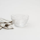 Pressed glass bowl with fleur de lit pattern and linen napkin on a white background