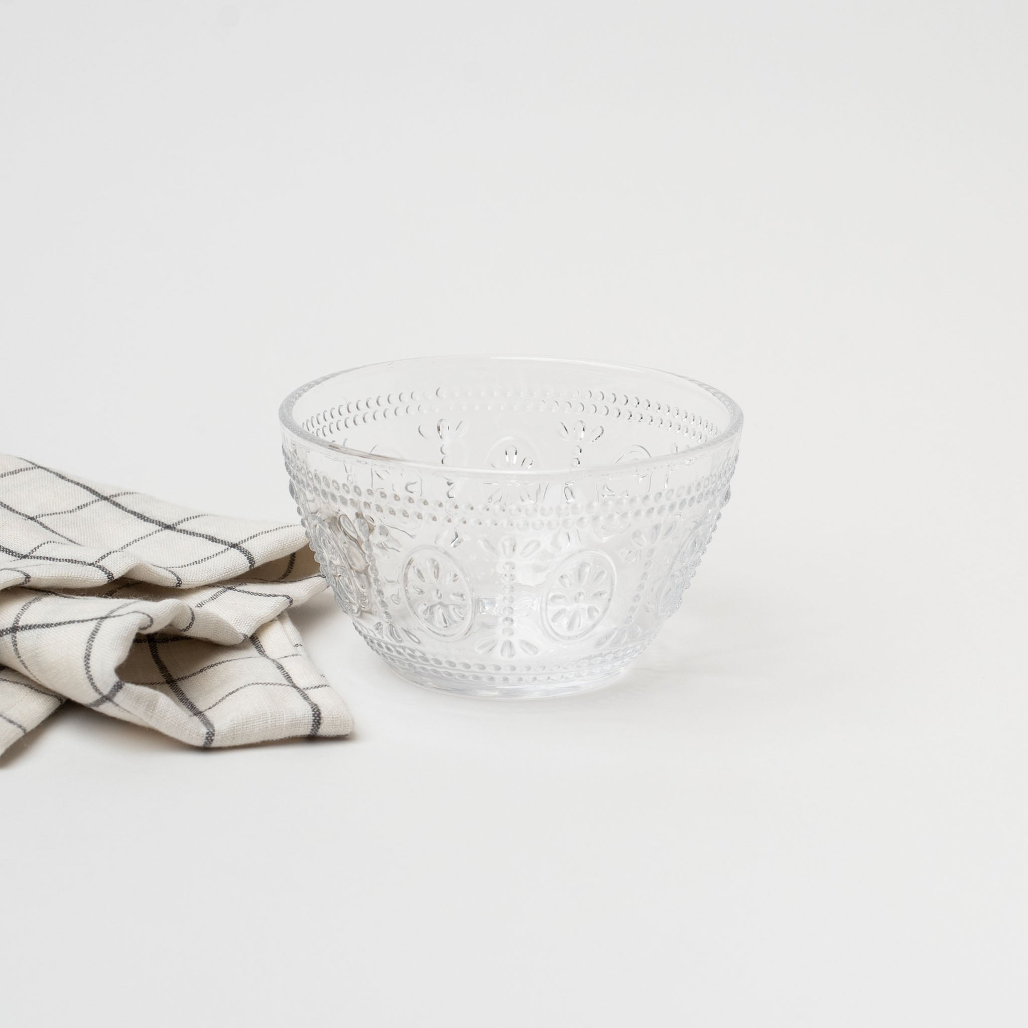 Pressed glass bowl with fleur de lit pattern and linen napkin on a white background