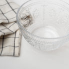 Close up of Pressed glass bowl with fleur de lit pattern and linen napkin on a white background