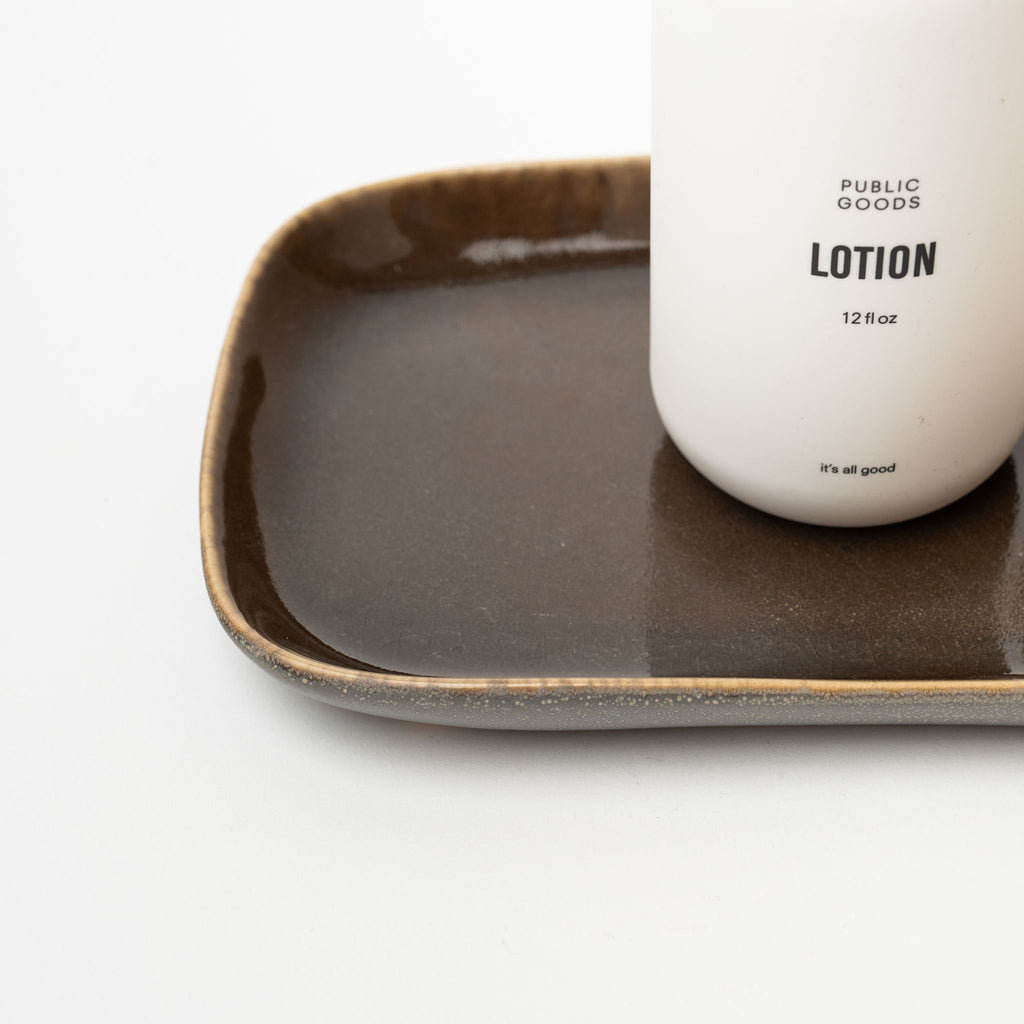 Brown stoneware tray with hand lotion bottle on top on a white background