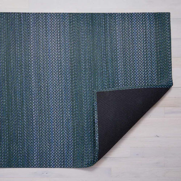 Chilewich quill woven floor mat in greenish blue on a light wood floor 