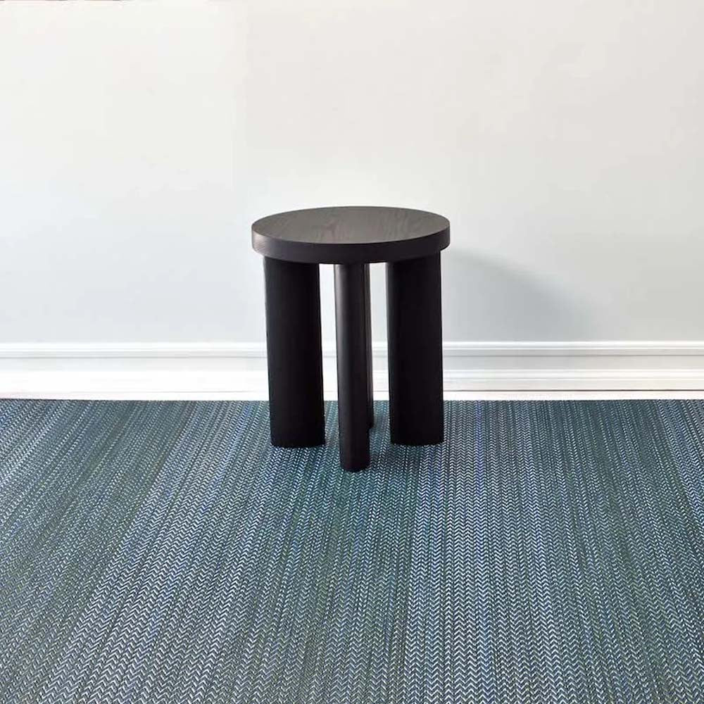 Chilewich quill woven floor mat in a room with white walls and black stool