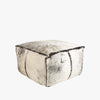 Square cow hide ottoman with blanket stitching on a white background