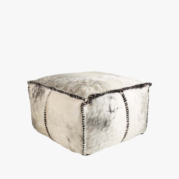 Square cow hide ottoman with blanket stitching on a white background