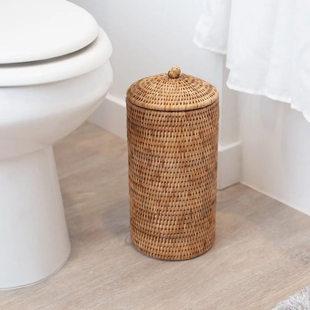 Rattan toilet paper holder with lid in white bathroom on floor by toilet 