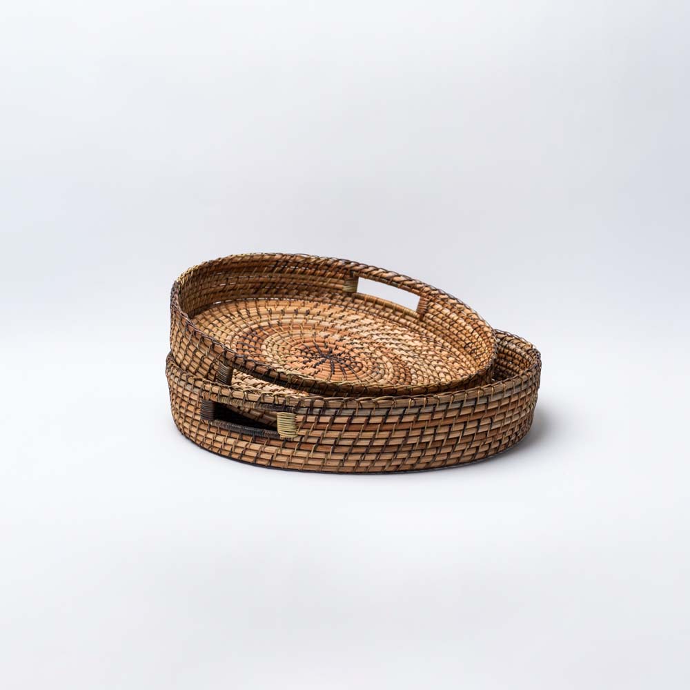 Two round rattan trays with handles by Bloomingville in two sizes on a white background