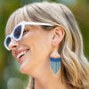 Model wearing Ink and alloy brand blue and coral color block earrings with white sunglasses