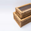 Close up of tops of two cane and rattan boxes with glass lids stacked on a white background