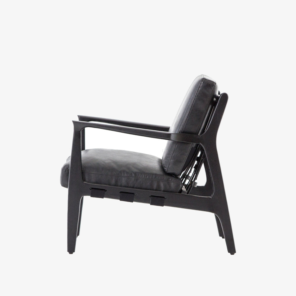 Side view of Four hands brand Silas arm chair with black wood frame and black leather cushions on a white background
