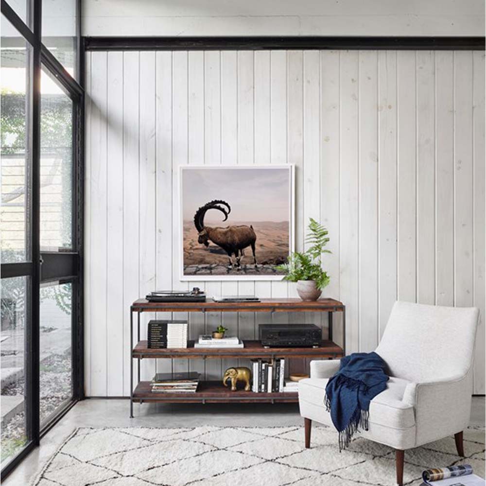 White living room with large black framed windows and four hands simian console with three shelves against white wall with photograph above