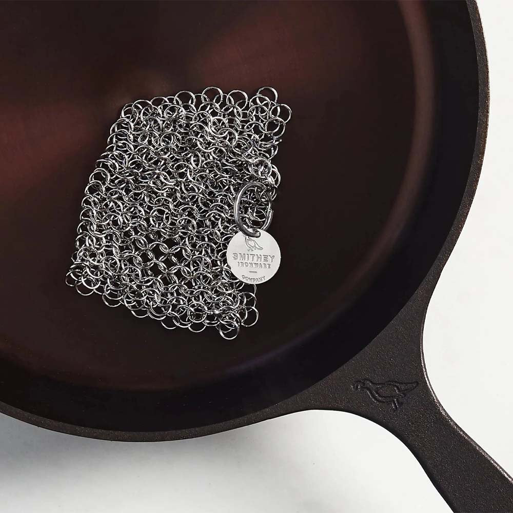 Smithey Chainmail Scrubber in a cast iron pan on a white background