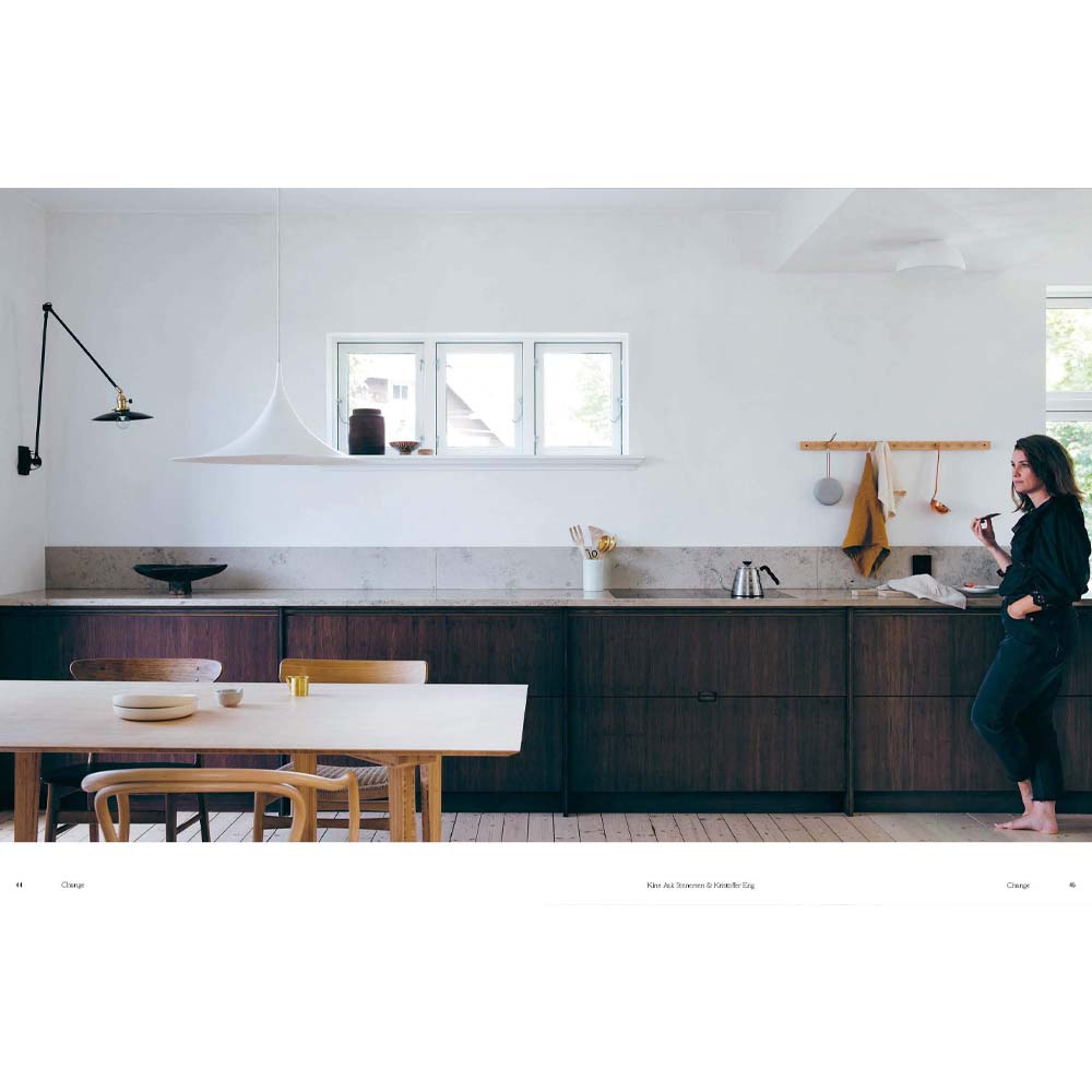 Photograph of a barefoot woman in a white and wood kitchen from the book: Still the slow home