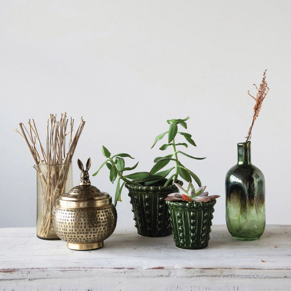 Two green planters with hobnail pattern on a wood surface with brass container and bottle 