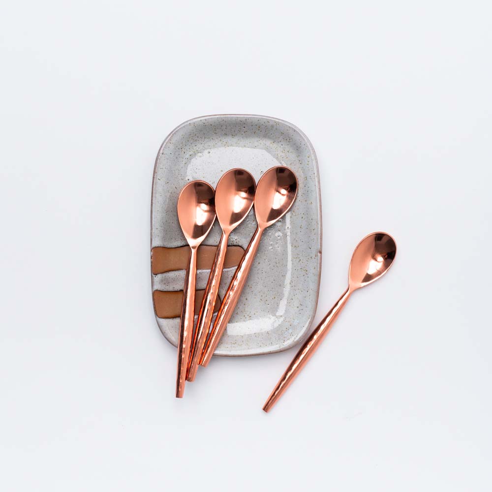 Set of four copper spoons on a small rectangular hand painted dish
