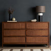Six drawer 'Sydney' dresser with brown cane stained drawers stained mango wood exterior by Four Hands Furniture in front of a charcoal grey wall with vase and lamp and other decorative items