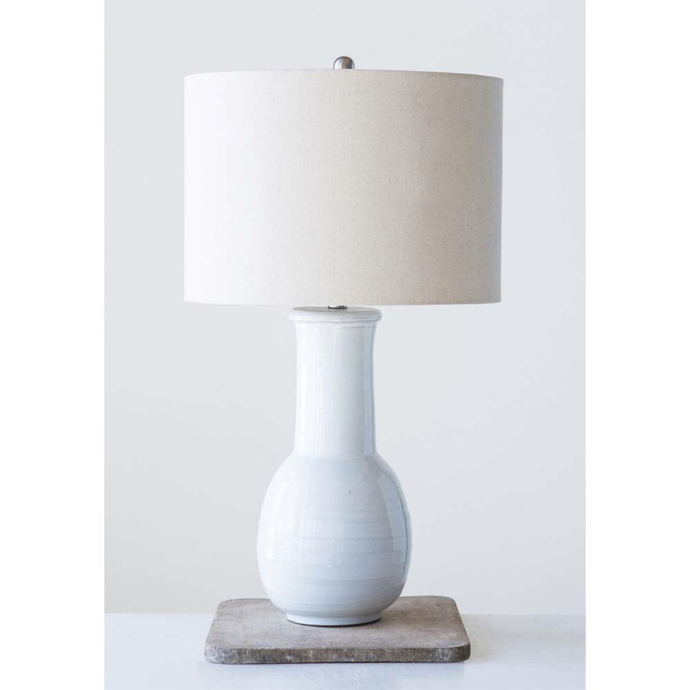Tall white terracotta lamp with linen shade  on a wood riser