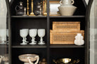 Two cane and rattan boxes by creative coop with glass lids in a black cabinet with other decorative items