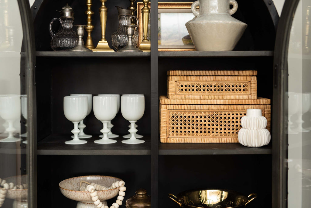 Two cane and rattan boxes by creative coop with glass lids in a black cabinet with other decorative items