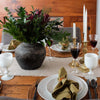 Wood dining table set for meal with natural linen table runner andlarge black vase with greenery