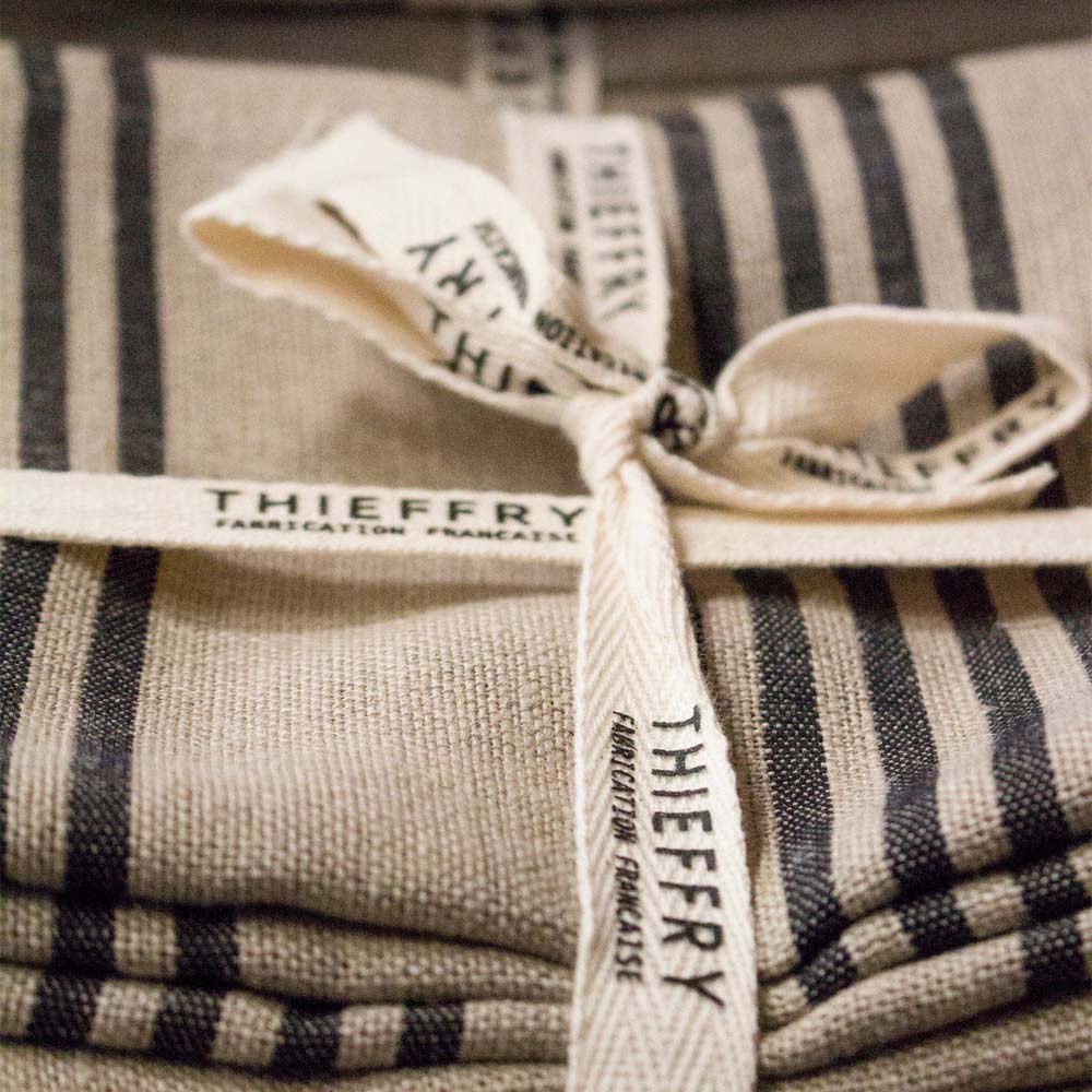 Close up of two natural with black stripe Thieffry Belgian Linen kitchen tea towels on a white background tied with a bow  